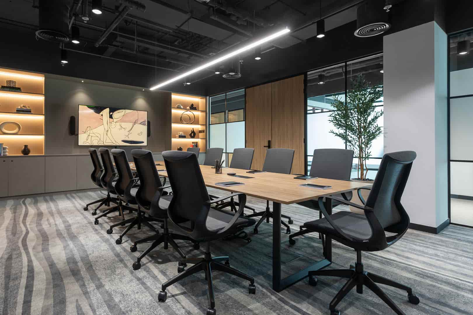 Modern boardroom with a long wooden table, black ergonomic chairs, and warm shelf lighting.