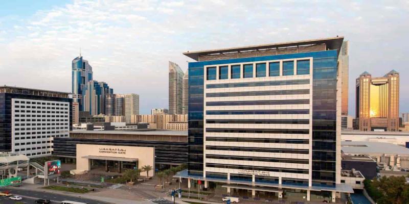 Modern cityscape with tall glass office buildings and a convention center in the foreground.
